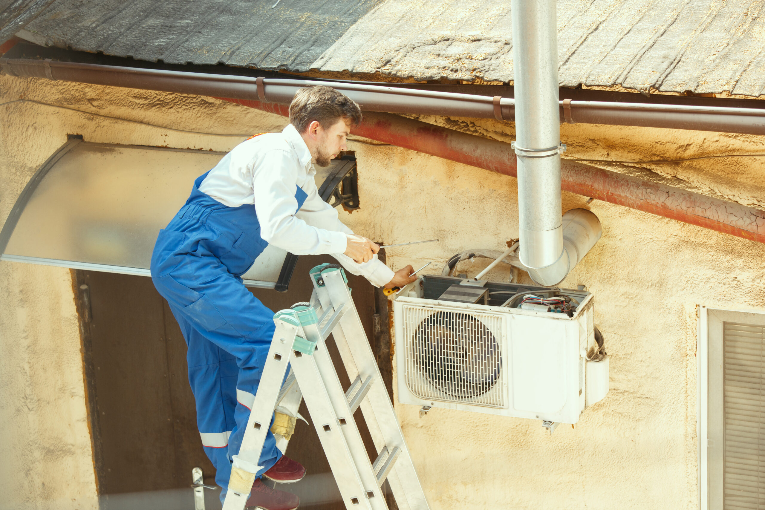 HVAC technician working on a capacitor part for condensing unit. Male worker or repairman in uniform repairing and adjusting conditioning system, diagnosting and looking for technical issues.